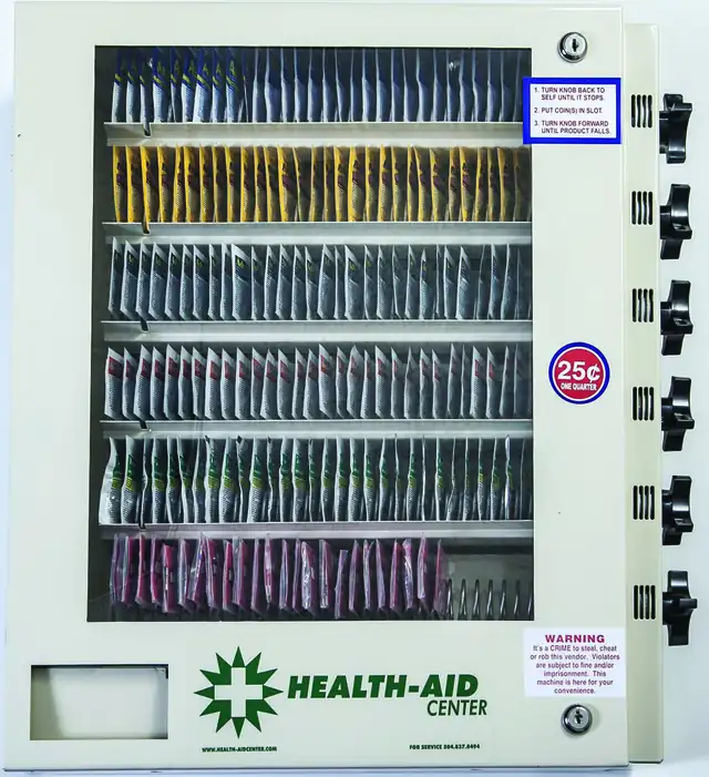 Health-Aid Center 6-Select — white powdercoated steel cabinet with coin mechanism, wall-mountable or with optional pedestal stand