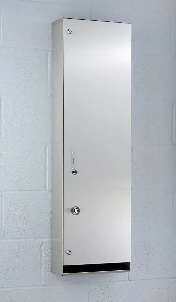 Slim stainless steel diaper vendor mounted on a painted block wall, with a keyed door and a lower dispensing chute