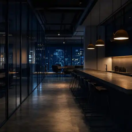 Corporate break room after hours — amber pendant light over an empty counter, city lights beyond the glass
